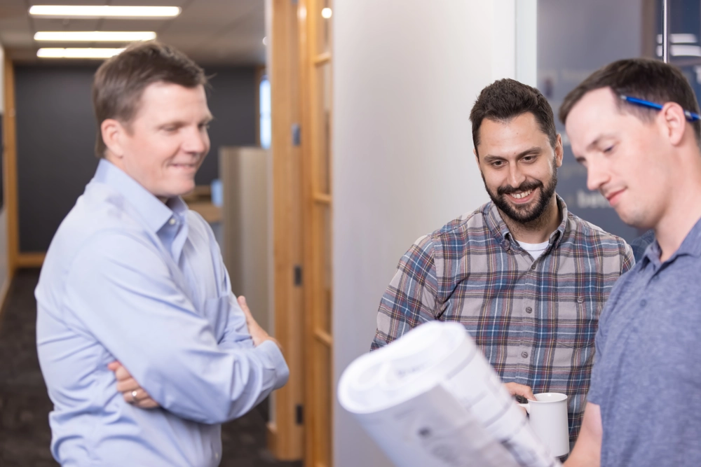 three men standing inside an office building looking a document held by a man on the right